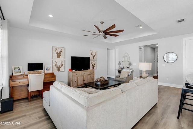 living room featuring ceiling fan, light wood-type flooring, and a tray ceiling