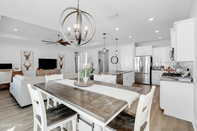 dining area with ceiling fan with notable chandelier, light hardwood / wood-style flooring, and sink