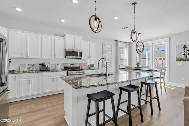 kitchen featuring appliances with stainless steel finishes, pendant lighting, white cabinetry, and sink