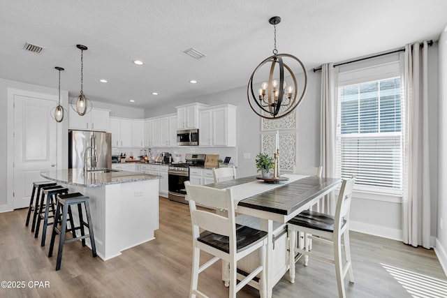 kitchen with a center island with sink, pendant lighting, white cabinetry, stainless steel appliances, and light stone counters