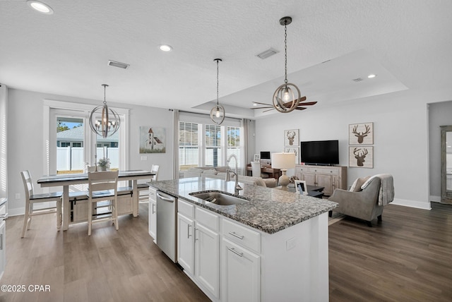 kitchen featuring decorative light fixtures, a center island with sink, sink, white cabinets, and dark stone counters