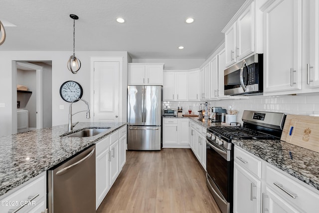 kitchen featuring white cabinets, appliances with stainless steel finishes, sink, hanging light fixtures, and stone counters