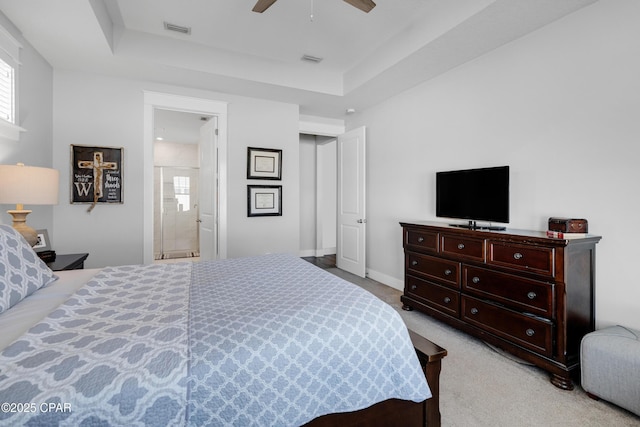 bedroom featuring ceiling fan, ensuite bathroom, light colored carpet, and a raised ceiling