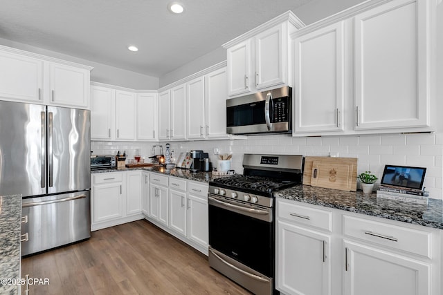 kitchen featuring stainless steel appliances, light hardwood / wood-style floors, white cabinets, and dark stone counters