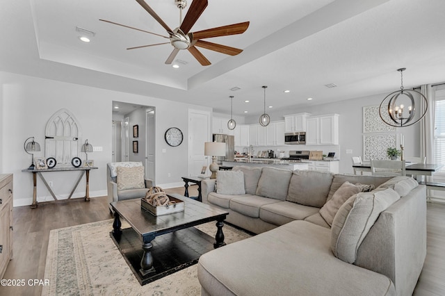 living room with a raised ceiling, ceiling fan with notable chandelier, and hardwood / wood-style floors