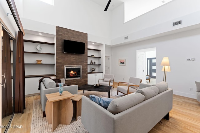 living room featuring a large fireplace, a towering ceiling, built in features, and light hardwood / wood-style flooring