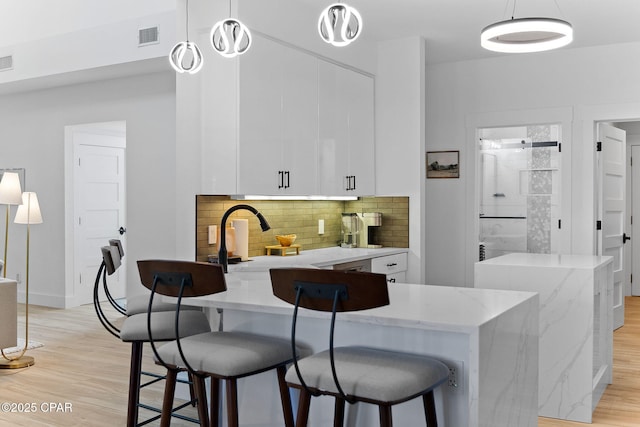 kitchen featuring decorative light fixtures, light wood-type flooring, white cabinetry, and backsplash