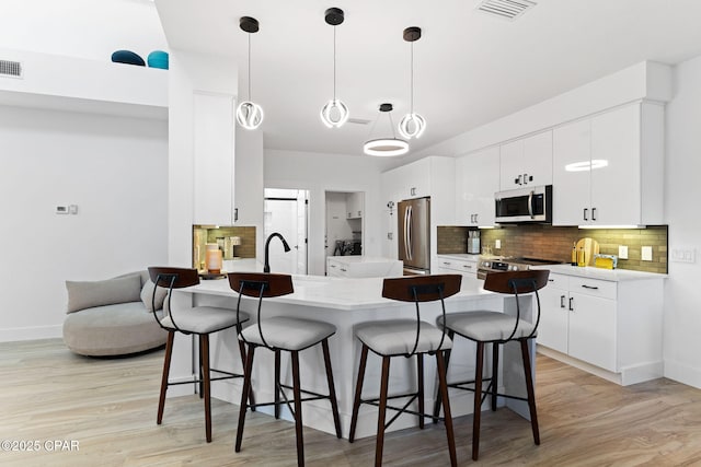 kitchen featuring white cabinets, pendant lighting, light wood-type flooring, and stainless steel appliances