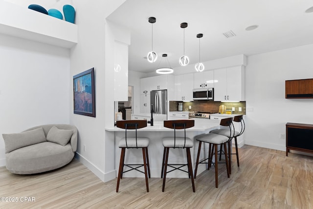 kitchen featuring pendant lighting, white cabinets, a breakfast bar area, kitchen peninsula, and stainless steel appliances