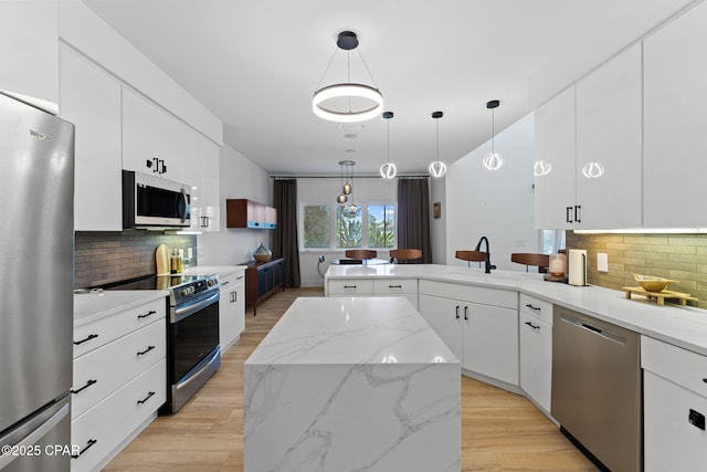 kitchen featuring white cabinetry, hanging light fixtures, stainless steel appliances, decorative backsplash, and a kitchen island