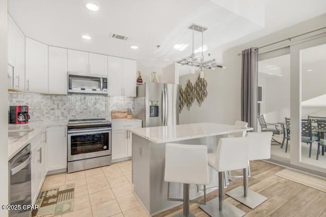 kitchen with a center island, hanging light fixtures, a kitchen breakfast bar, white cabinets, and appliances with stainless steel finishes