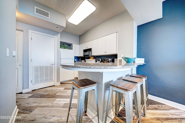 kitchen with light hardwood / wood-style floors, white fridge, white cabinetry, a kitchen bar, and kitchen peninsula