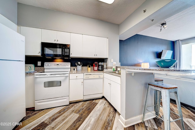 kitchen with kitchen peninsula, white appliances, white cabinets, and a breakfast bar area