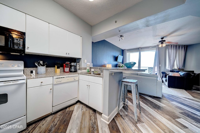 kitchen with white appliances, white cabinetry, a breakfast bar, and kitchen peninsula