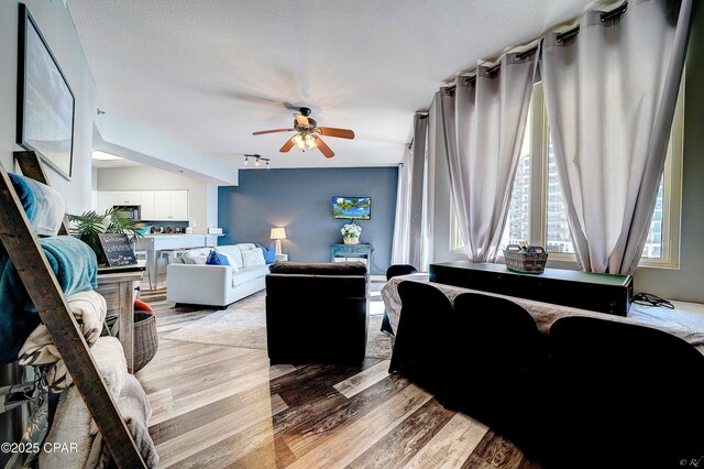 living room with ceiling fan, a textured ceiling, and light wood-type flooring