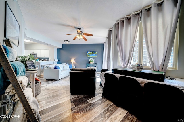 living room with ceiling fan, a textured ceiling, and light hardwood / wood-style floors