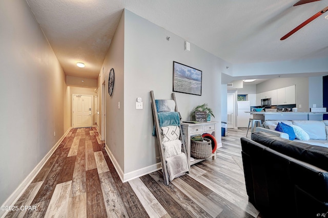 corridor featuring ceiling fan, light hardwood / wood-style flooring, and a textured ceiling