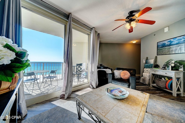 living room featuring a textured ceiling, dark wood-type flooring, a water view, and ceiling fan