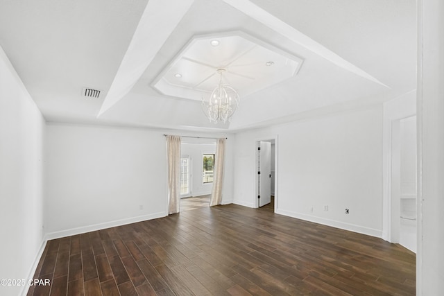 spare room featuring visible vents, a notable chandelier, a tray ceiling, dark wood-style floors, and baseboards