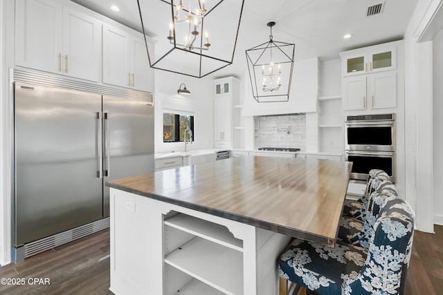 kitchen with visible vents, dark wood finished floors, an inviting chandelier, stainless steel appliances, and glass insert cabinets