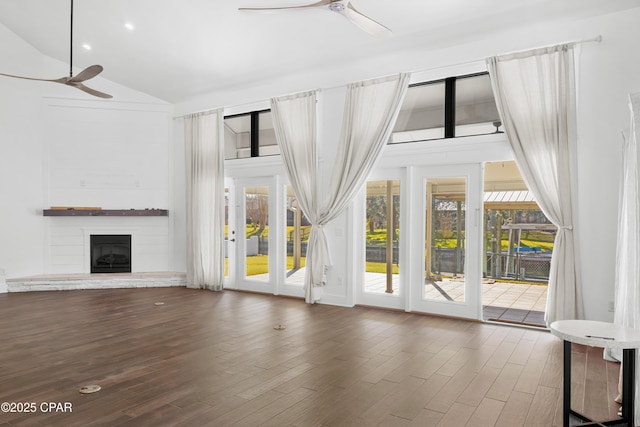 unfurnished living room with lofted ceiling, a fireplace with raised hearth, wood finished floors, and ceiling fan