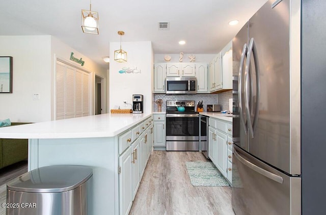 kitchen featuring a kitchen bar, tasteful backsplash, stainless steel appliances, light hardwood / wood-style floors, and hanging light fixtures