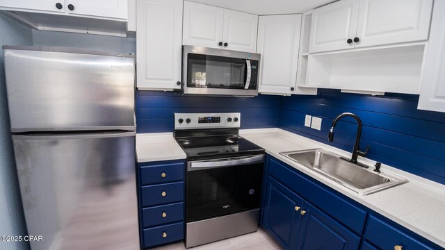 kitchen with stainless steel appliances, blue cabinetry, sink, and white cabinets