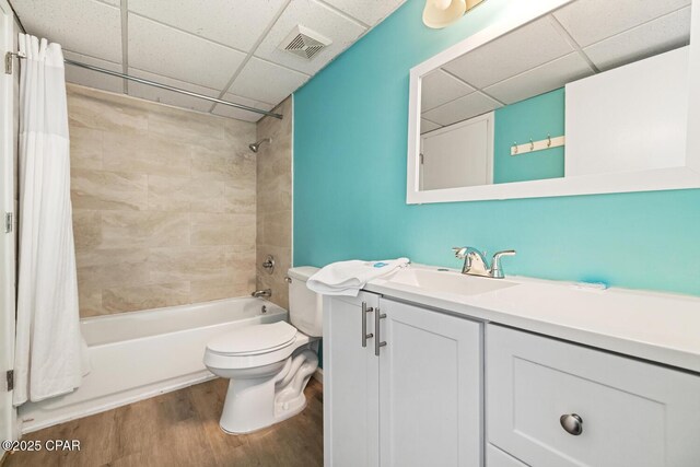 full bathroom with a drop ceiling, hardwood / wood-style floors, toilet, shower / bath combination with curtain, and vanity