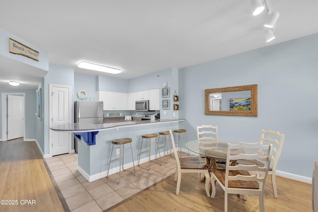 kitchen with white cabinetry, a kitchen breakfast bar, kitchen peninsula, stainless steel appliances, and light wood-type flooring