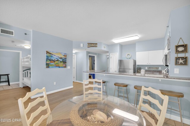 kitchen featuring a kitchen breakfast bar, light hardwood / wood-style floors, stainless steel appliances, kitchen peninsula, and white cabinets