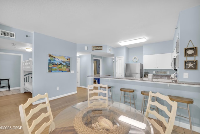 kitchen with appliances with stainless steel finishes, light hardwood / wood-style floors, white cabinets, a kitchen bar, and kitchen peninsula