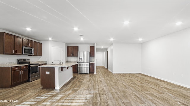 kitchen featuring sink, a center island with sink, light hardwood / wood-style flooring, a kitchen breakfast bar, and stainless steel appliances