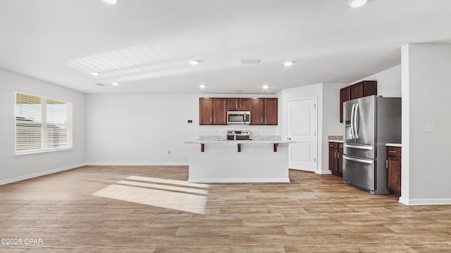 kitchen featuring a kitchen island with sink, a kitchen bar, light wood-type flooring, and appliances with stainless steel finishes