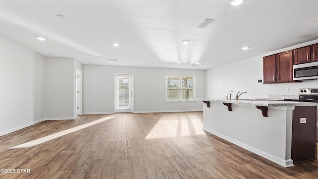 kitchen featuring stainless steel appliances, a kitchen bar, dark hardwood / wood-style flooring, and a kitchen island with sink