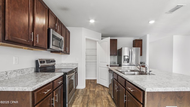 kitchen with sink, dark brown cabinets, dark hardwood / wood-style floors, stainless steel appliances, and a kitchen island with sink