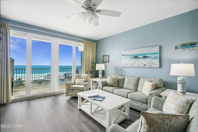 living room with a water view, hardwood / wood-style floors, ceiling fan, and a view of the beach