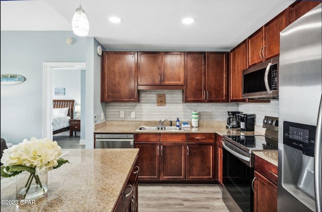 kitchen featuring appliances with stainless steel finishes, pendant lighting, sink, backsplash, and light stone countertops