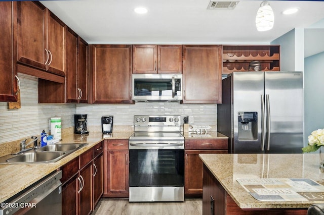 kitchen with sink, light stone counters, pendant lighting, stainless steel appliances, and decorative backsplash