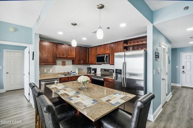 kitchen featuring light stone counters, hanging light fixtures, a breakfast bar area, and stainless steel appliances