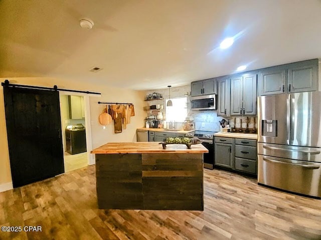 kitchen featuring butcher block countertops, a barn door, light hardwood / wood-style flooring, and stainless steel appliances