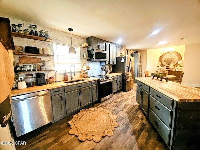 kitchen featuring wood counters, stainless steel appliances, sink, pendant lighting, and dark hardwood / wood-style floors