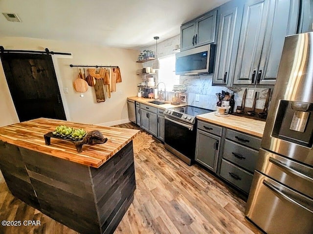 kitchen with a barn door, sink, wooden counters, and appliances with stainless steel finishes