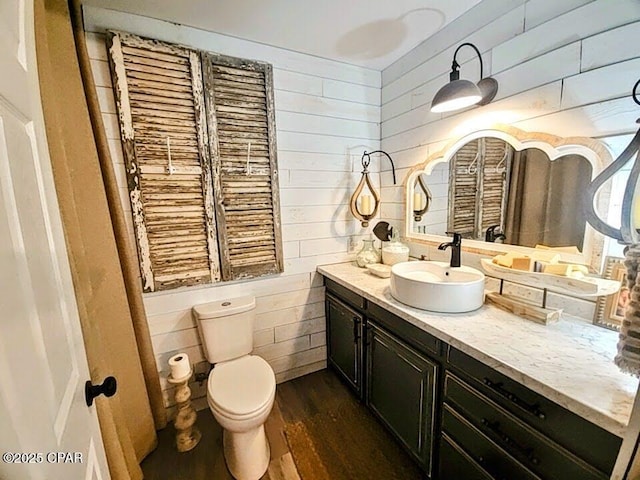 bathroom featuring wood-type flooring, vanity, toilet, and wooden walls