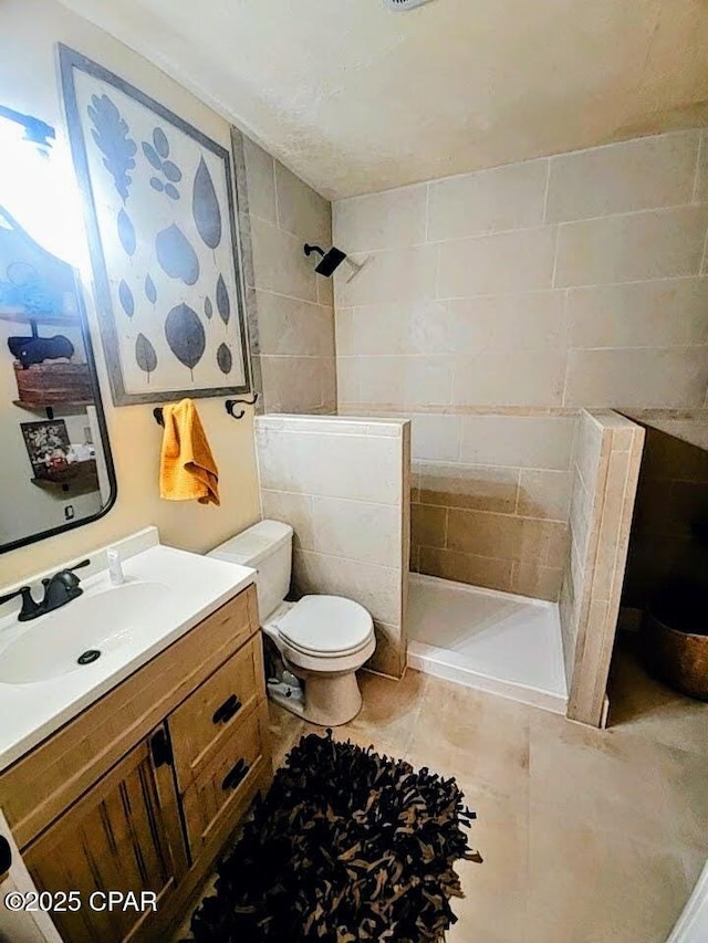 bathroom with tile patterned floors, vanity, toilet, and a tile shower