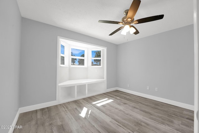 empty room featuring ceiling fan, a textured ceiling, wood finished floors, and baseboards