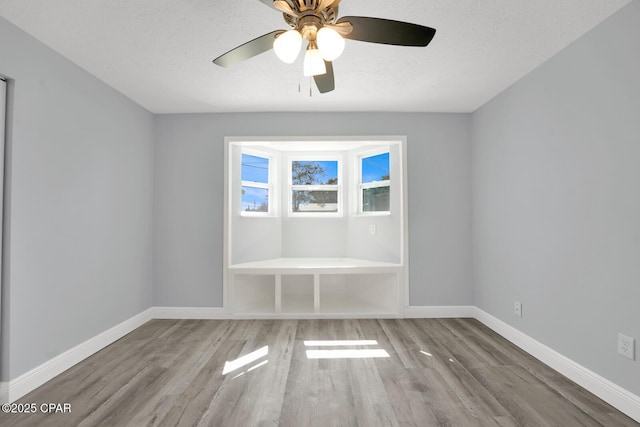 empty room with a textured ceiling, wood finished floors, a ceiling fan, and baseboards