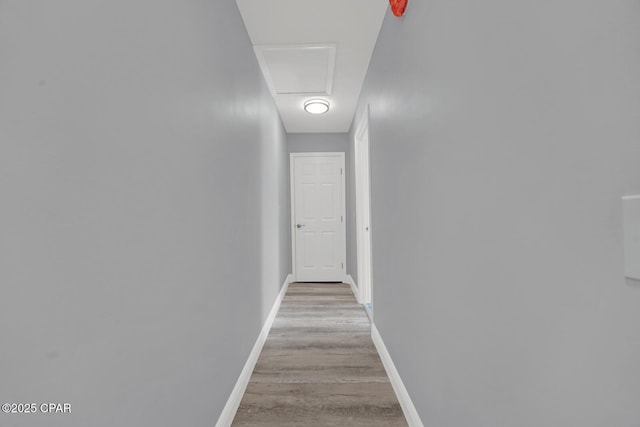 hallway featuring light wood-style floors, attic access, and baseboards