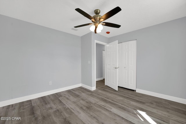 unfurnished bedroom with a closet, wood finished floors, a ceiling fan, and baseboards