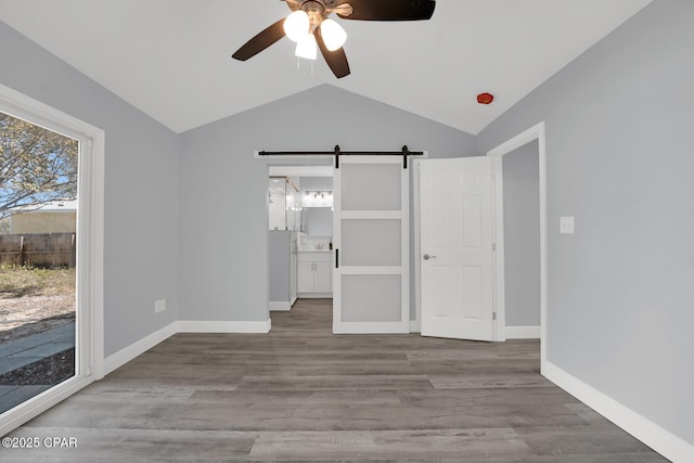 unfurnished bedroom with a barn door, wood finished floors, baseboards, vaulted ceiling, and access to outside