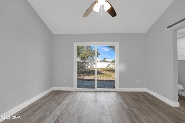 spare room with ceiling fan, a barn door, wood finished floors, and baseboards